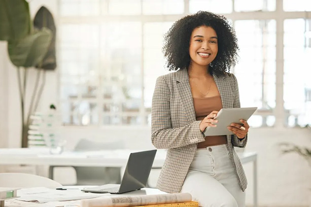 Picture of a young professional woman at a desk holding papers and smiling at the camera.